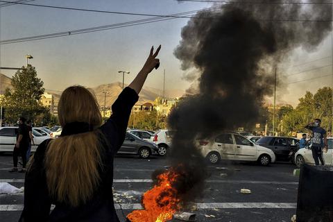 Eine Frau steht während einer Demonstration in Teheran nach dem Tod der 22-jährigen Mahsa Amini vor einem brennenden Autoreifen und macht das Victory-Zeichen.  