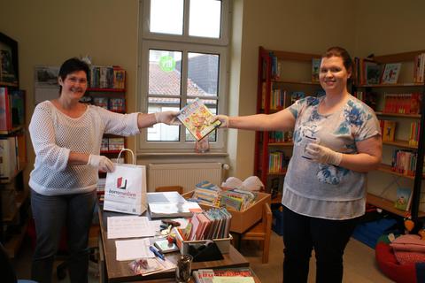 Viel Abstand zueinander, Handschuhe und eine kontaktlose Übergabe: Viktoria Steffen (links) und Rita Hasslinger beachten alle Maßgaben bei ihrer Buchlieferung. Foto: Laura Schöffel